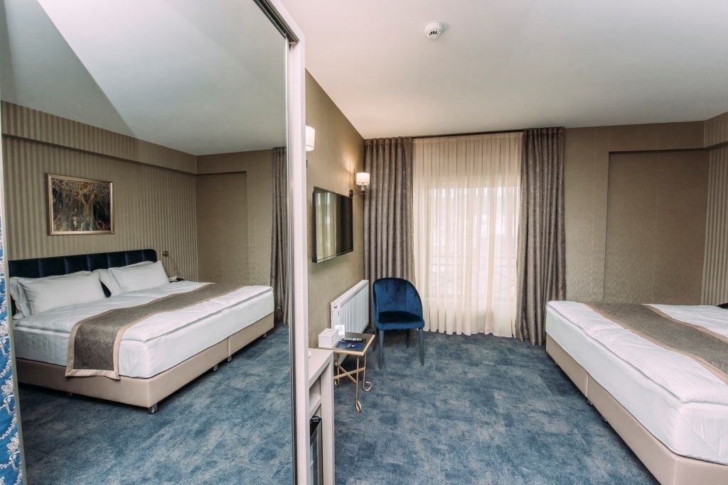 Habitación de hotel con dos camas, un escritorio, una silla y un ventanal con cortinas.