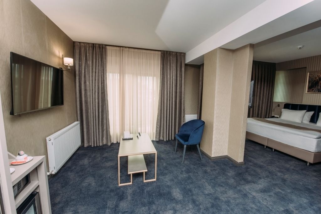 Habitación de hotel con cama, escritorio, silla, televisión y ventana con cortinas.