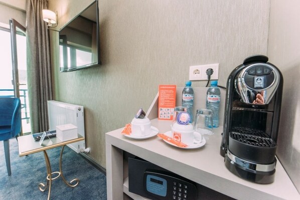 A hotel room with a coffee maker, water bottles, a glass of water, a remote control, and a television mounted on the wall. - Hotel Sapphire Bakuriani (Borjomi)