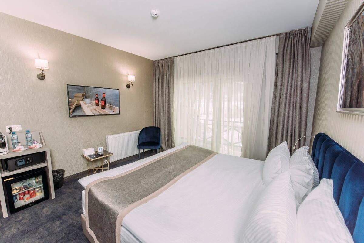 Ein Hotelzimmer mit einem Bett, einem Schreibtisch mit Computer, einem Kühlschrank und einem Fenster mit Vorhängen.