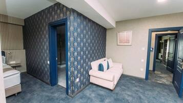 Une pièce avec un papier peint bleu et blanc à motifs, un canapé blanc agrémenté de coussins bleus, un lit recouvert d’une couverture à rayures et un tableau encadré accroché au mur.