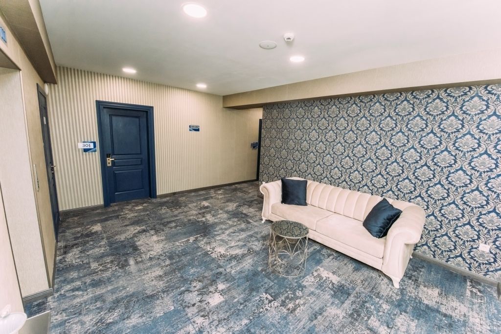 Una habitación con un sofá color beige, un papel tapiz estampado y una puerta azul.