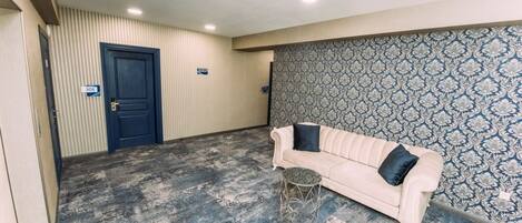 Una habitación con un sofá color beige, un papel tapiz estampado y una puerta azul.