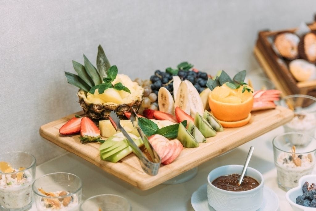 A wooden board with various fruits and a bowl of chocolate spread.