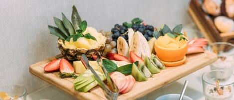 A wooden board with various fruits and a bowl of chocolate spread.