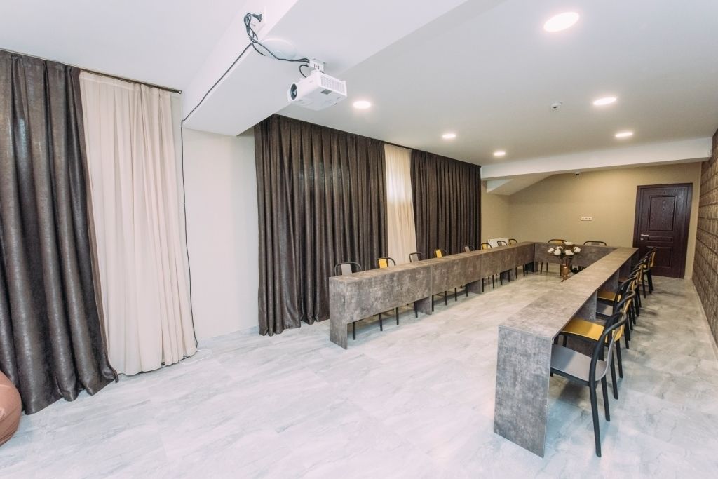 A spacious room with a long table and chairs, a projector, and curtains.