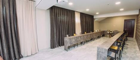 A spacious room with a long table and chairs, a projector, and curtains.