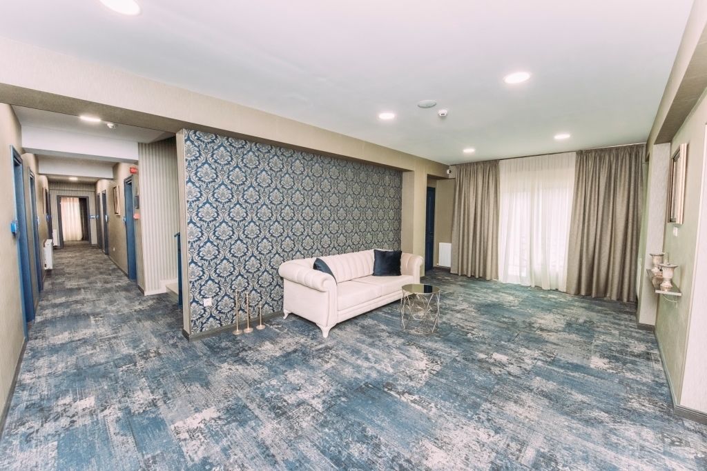 A hotel room with a patterned wall, a beige sofa, and a blue carpet.
