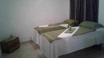 Two single beds with white sheets and green blankets, a nightstand with a lamp, and a window with curtains.