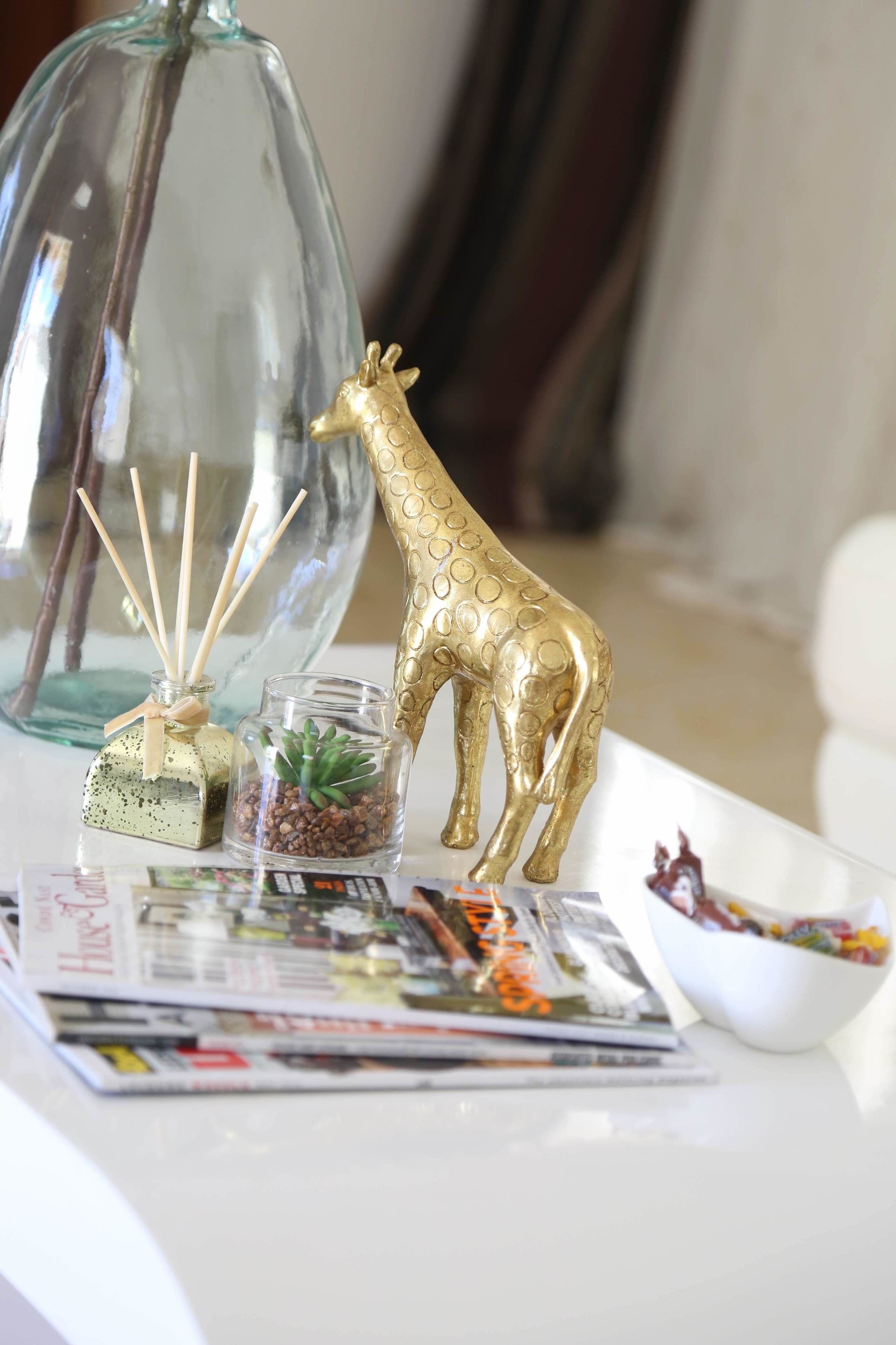 A table with a decorative glass vase, a golden giraffe figurine, a small glass terrarium, and a bowl of candy.