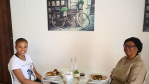 Two people seated at a round glass table with plates of food, a coffee cup, and salt and pepper shakers. - Denver Echo- Executive Guest House (Maseru)