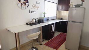 A compact kitchen with a white countertop, a stainless steel bar stool, a refrigerator, and a red rug. - Denver Echo- Executive Guest House (Maseru)