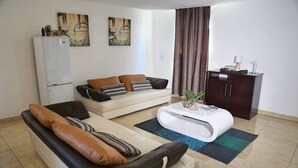 A modern living room with a sofa, a coffee table, a cabinet, and artwork on the wall. - Denver Echo- Executive Guest House (Maseru)