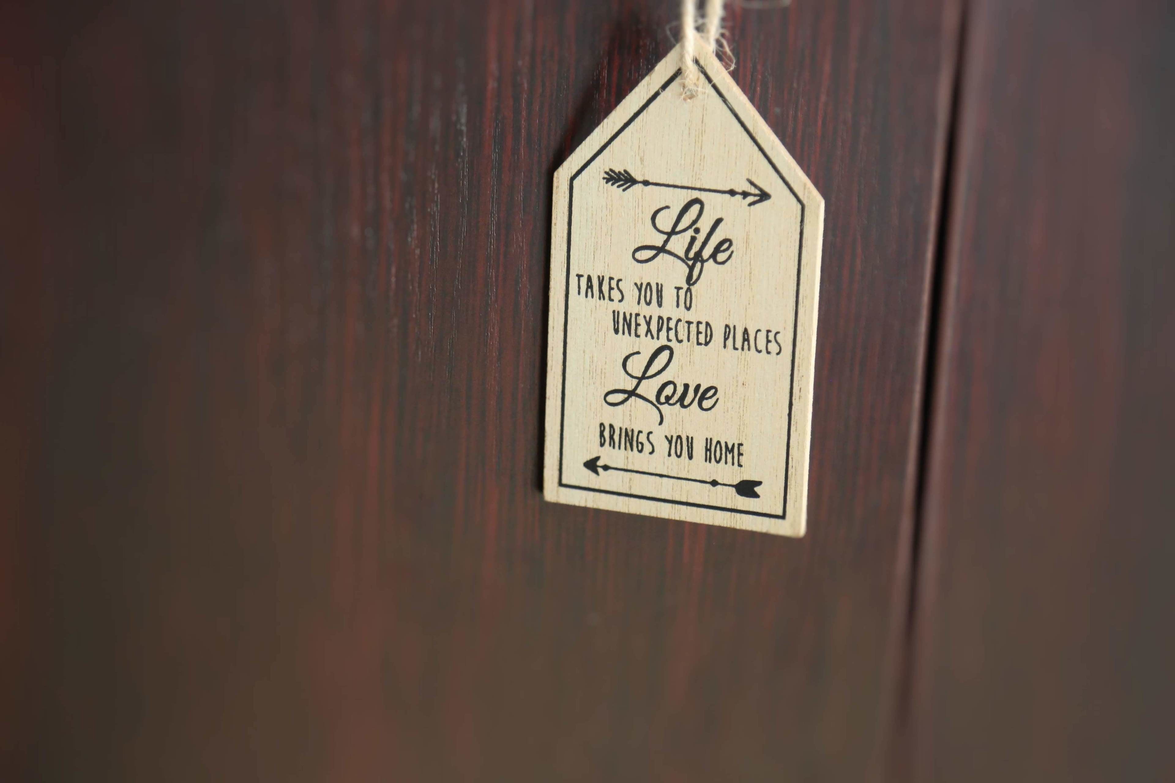 Un letrero de madera con el texto: 'La vida te lleva a lugares inesperados, el amor te trae de vuelta a casa.'
