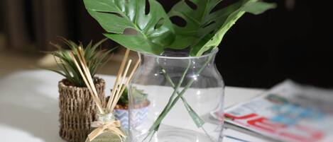 A clear glass vase with a single green plant, a small potted plant, and a decorative item with a ribbon on a table.