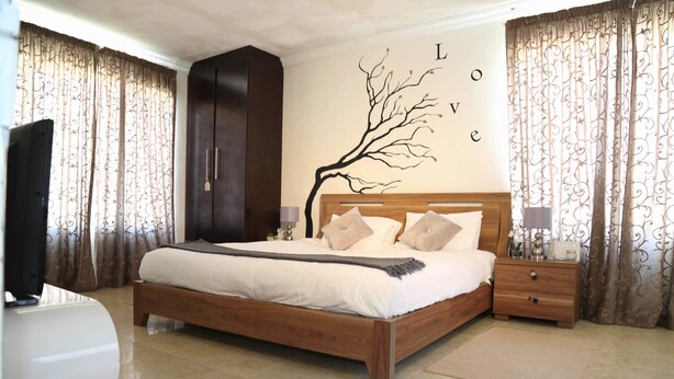 A bedroom with a wooden bed, a wardrobe, a nightstand, and a TV. - Denver Echo- Executive Guest House (Maseru)