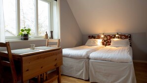 A bedroom with a wooden desk, two beds, a window with a view of trees, and a patterned headboard. - Ljungs Fem Rum (Gotlands Tofta)
