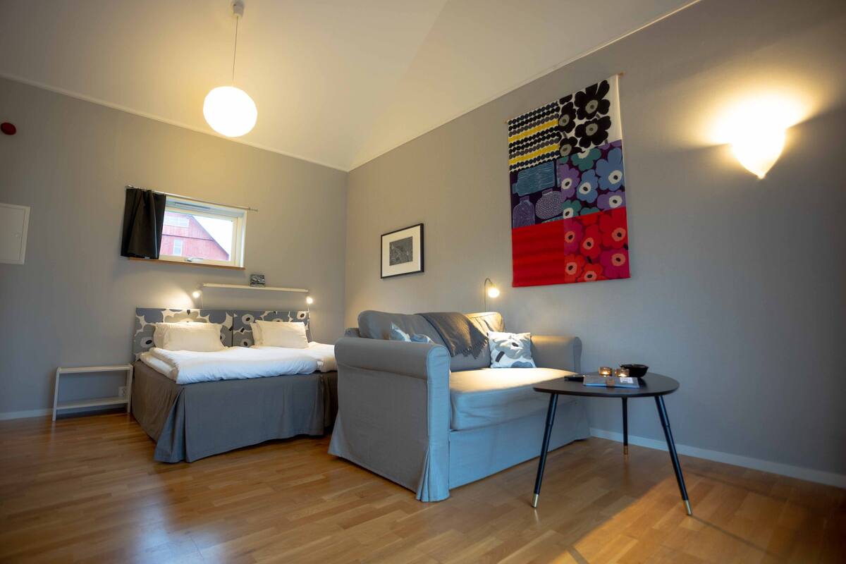 Ein modernes, helles Zimmer mit einem Bett, einem Sofa, einem kleinen Tisch und einem großen, abstrakten Gemälde an der Wand.