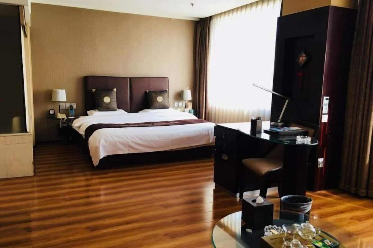 Une chambre d’hôtel avec un grand lit, un bureau avec une chaise, une télévision et une table à manger avec des chaises.