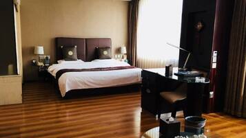 Een hotelkamer met een groot bed, een bureau met stoel, een televisie en een eettafel met stoelen.
