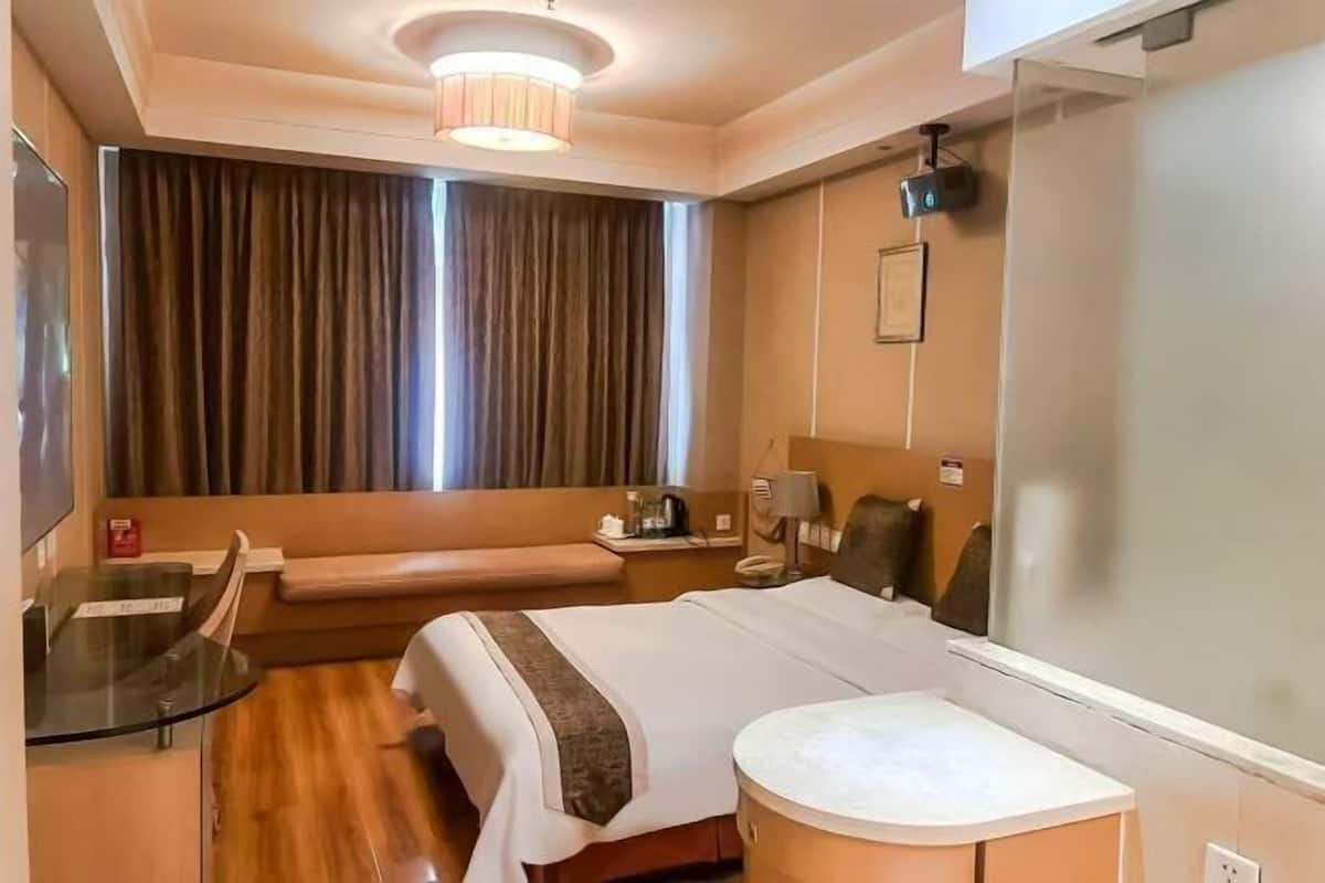 Une chambre d’hôtel comprenant un lit, une table de chevet, une lampe, un miroir, une fenêtre avec des rideaux et un petit coin salon.
