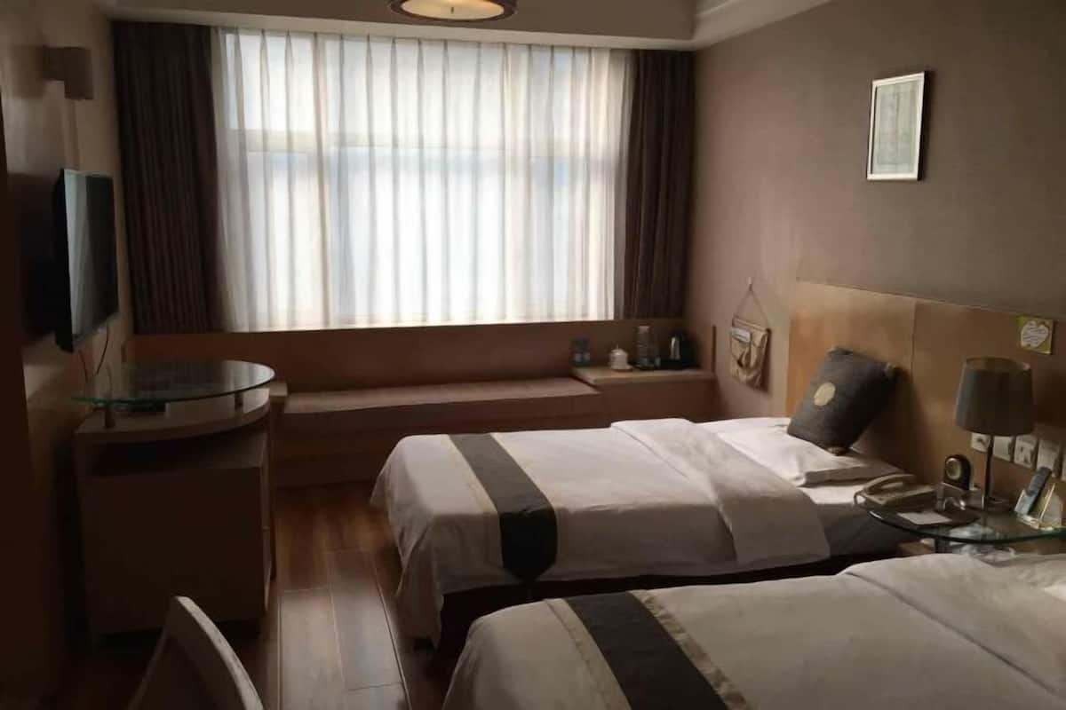 Une chambre d’hôtel avec deux lits, une télévision, une table de chevet, une lampe et une fenêtre avec des rideaux.