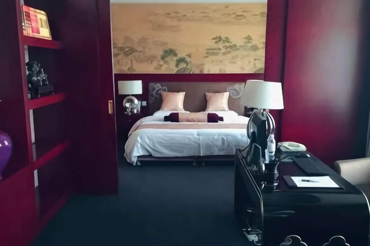 Une chambre d’hôtel avec un lit, des tables de chevet, un bureau et une armoire rouge.