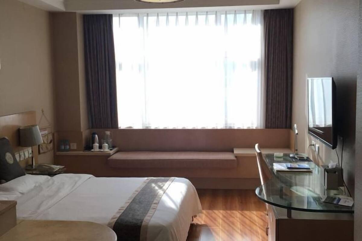 Une chambre d’hôtel avec un grand lit, un bureau, une télévision et une fenêtre avec des rideaux.