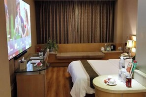 A hotel room with a bed, a sofa, a TV, a desk, and a bedside table with amenities. - Oceanwide Hotel (Weifang)