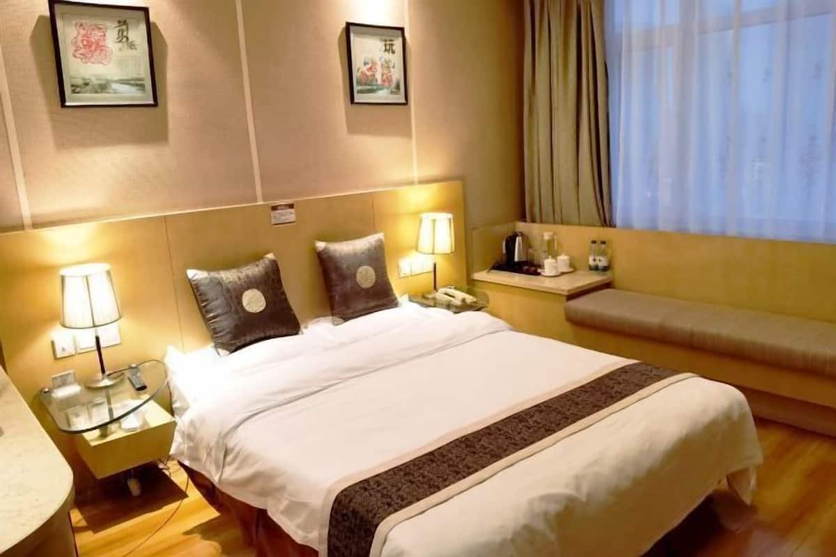 Une chambre d’hôtel comprenant un lit, des lampes de chevet, une table de chevet avec un téléphone, une petite table avec une bouilloire et une fenêtre avec des rideaux.