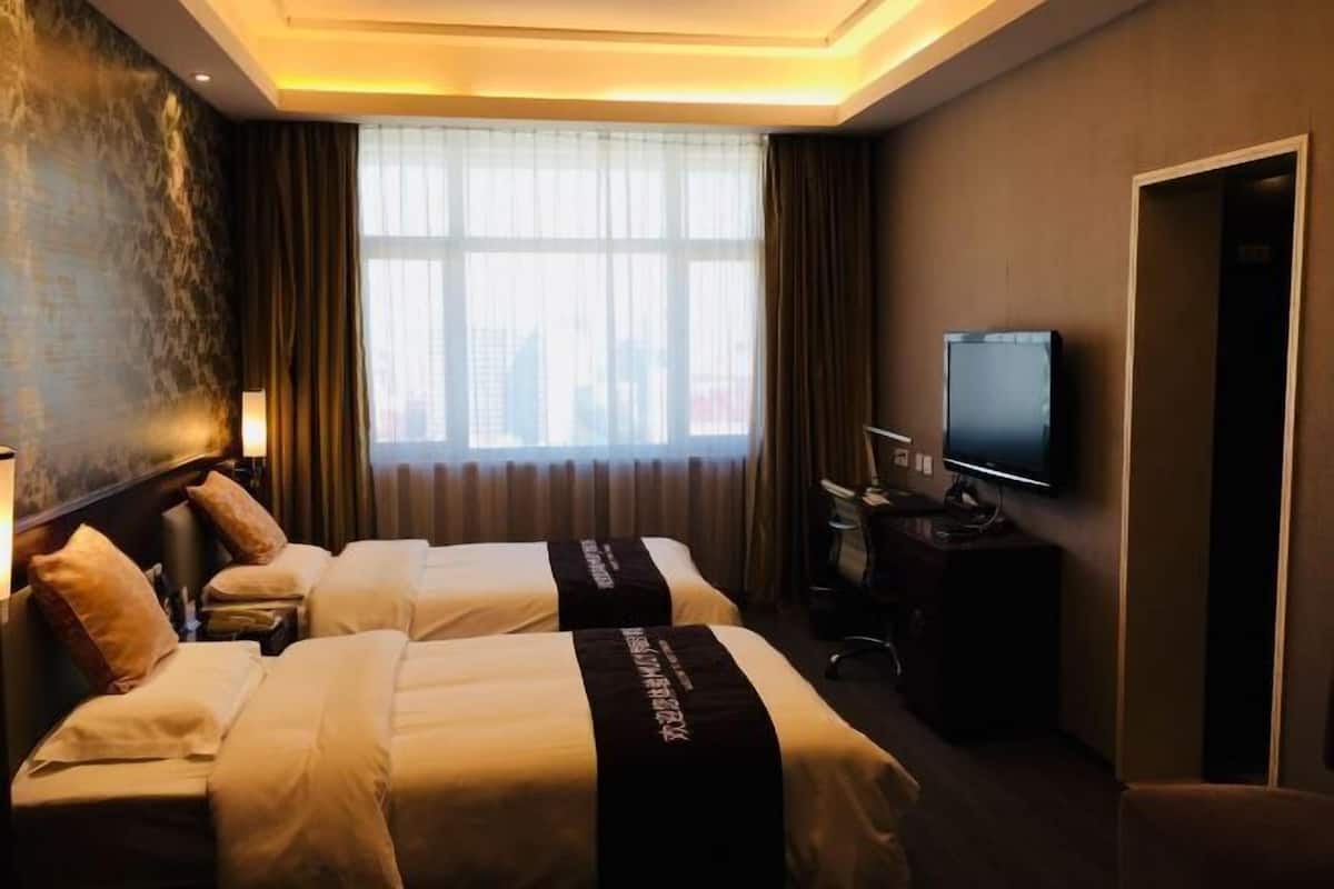 Une chambre d’hôtel avec deux lits, une télévision, un bureau et une fenêtre avec des rideaux.