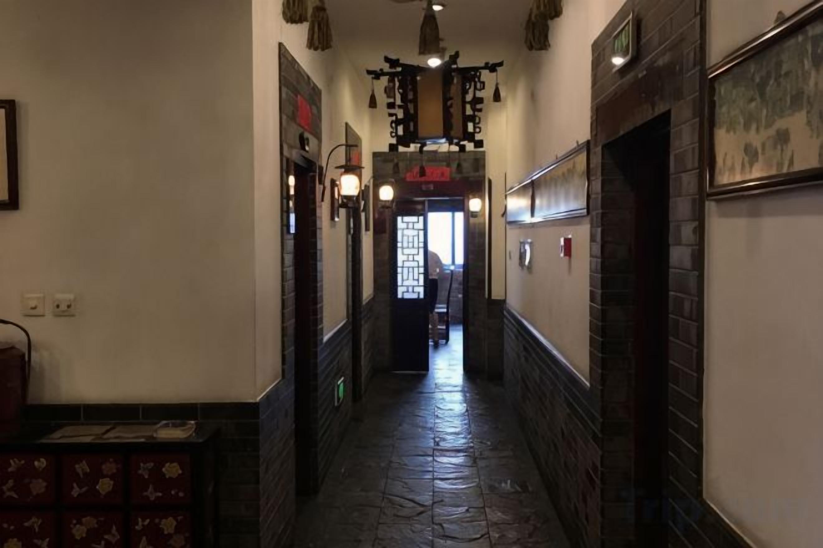 A narrow hallway with a tiled floor, a door at the end, and a wall-mounted light fixture.