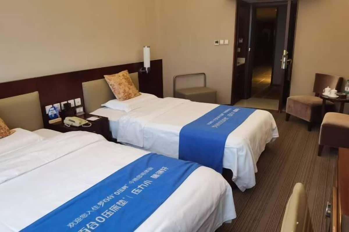 Une chambre d’hôtel avec deux lits, une chaise, un bureau et une porte donnant sur une autre pièce.