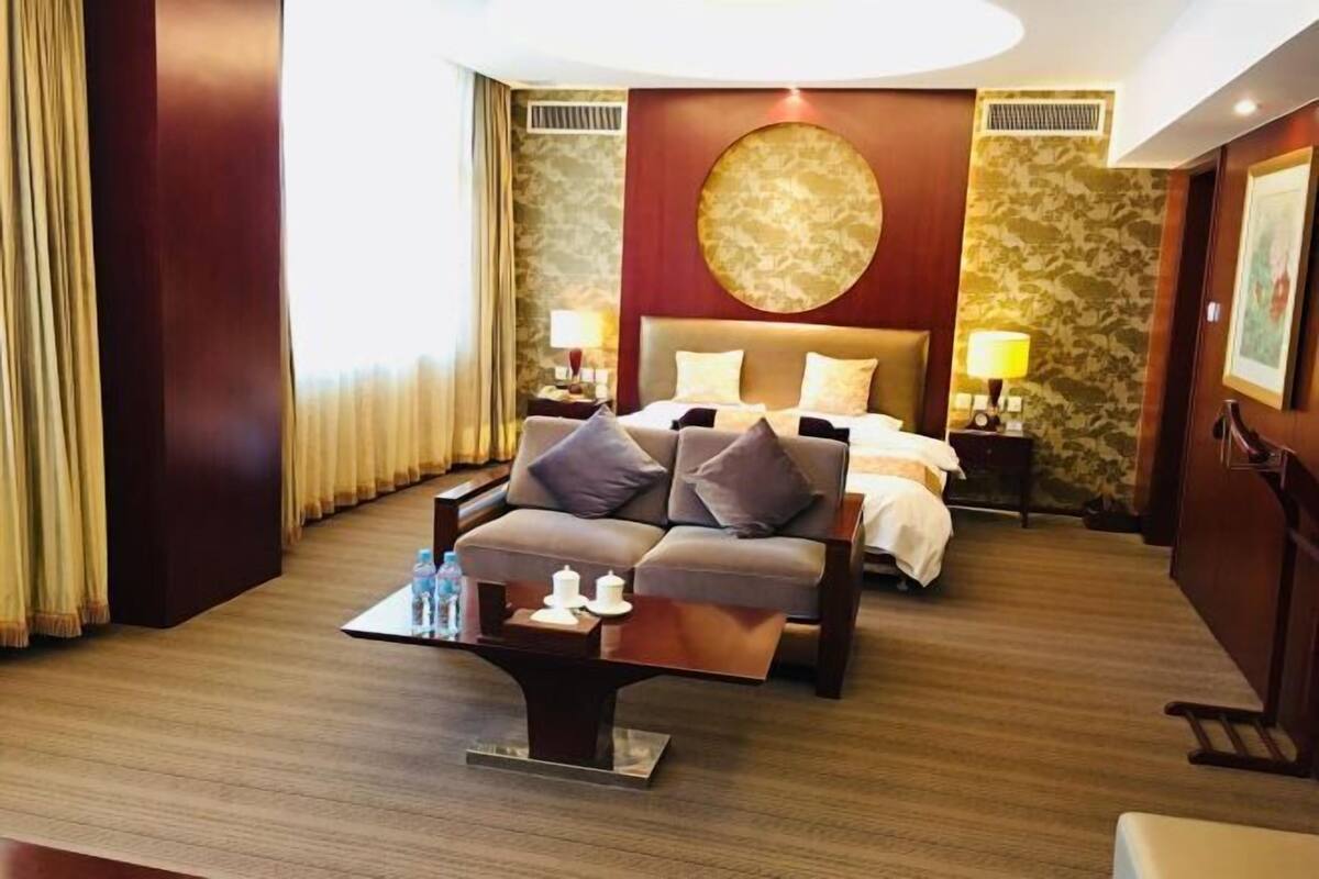 Une chambre d’hôtel avec un canapé-lit, une table de chevet avec une lampe, un grand élément décoratif circulaire fixé au mur et un papier peint à motifs.