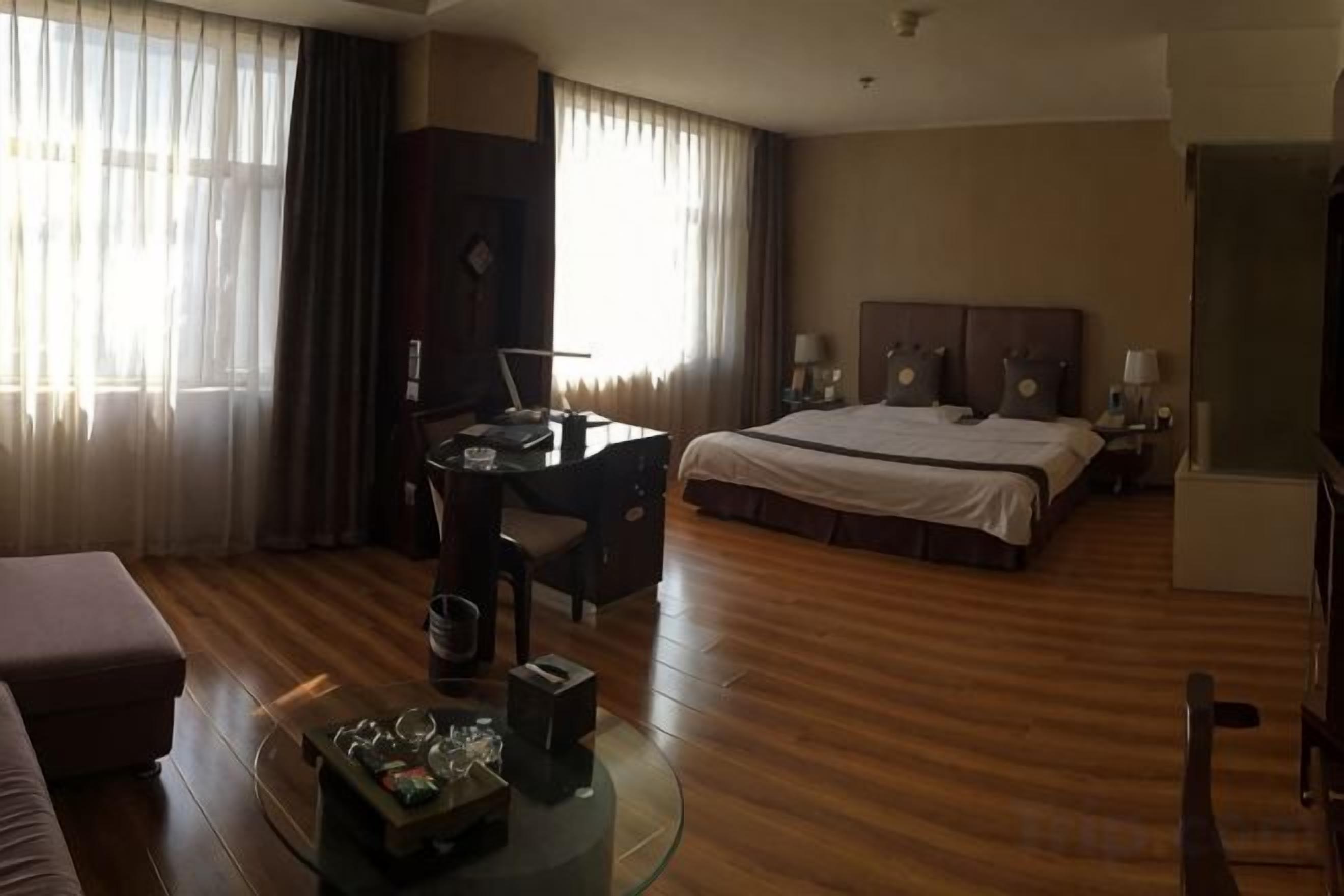 A hotel room with a bed, a desk, a chair, a glass coffee table, and a sofa.