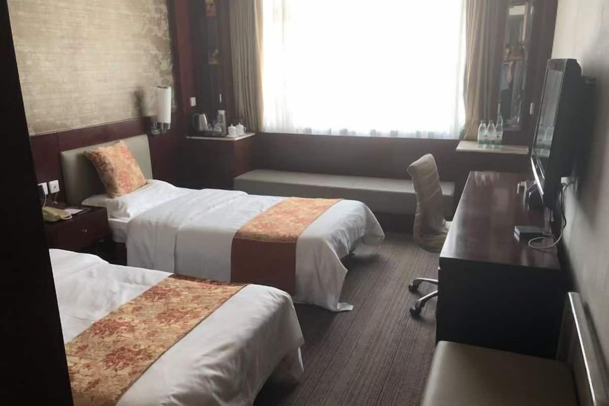 Une chambre d’hôtel avec deux lits, un bureau, une chaise, une télévision et une fenêtre avec des rideaux.