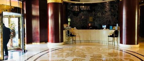 Un hall de hotel con una mesa de recepción, grandes columnas y un suelo estampado.
