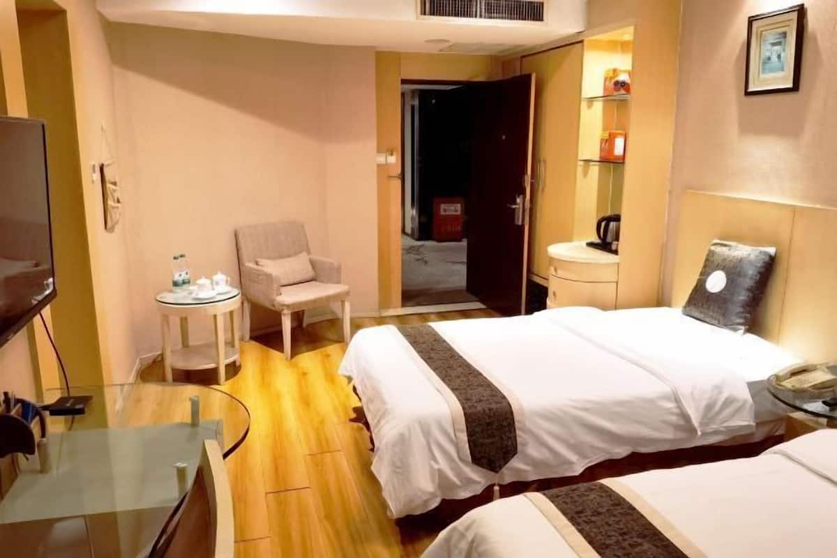 Une chambre d’hôtel avec deux lits, une petite table, une chaise, un bureau, un miroir et une porte donnant sur un balcon.