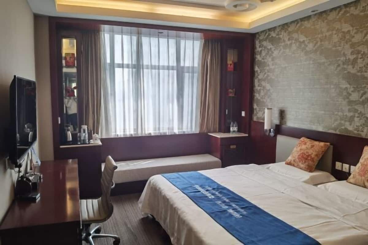 Une chambre d’hôtel avec un grand lit, un bureau, une chaise, une télévision et une fenêtre avec des rideaux.