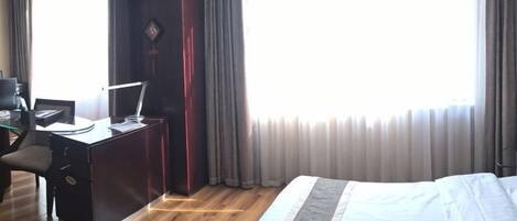 A hotel room with a bed, desk, chair, and curtains.