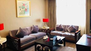 A hotel room with two sofas, a coffee table, a lamp, a painting, and a window with curtains. - Oceanwide Hotel (Weifang)