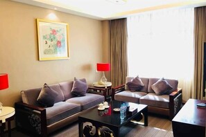 A hotel room with two sofas, a coffee table, a lamp, a painting, and a window with curtains. - Oceanwide Hotel (Weifang)
