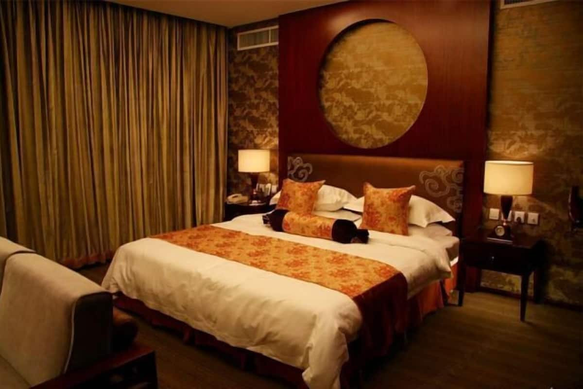 Une chambre d’hôtel avec un grand lit, deux tables de chevet, une chaise et une grande fenêtre avec des rideaux.