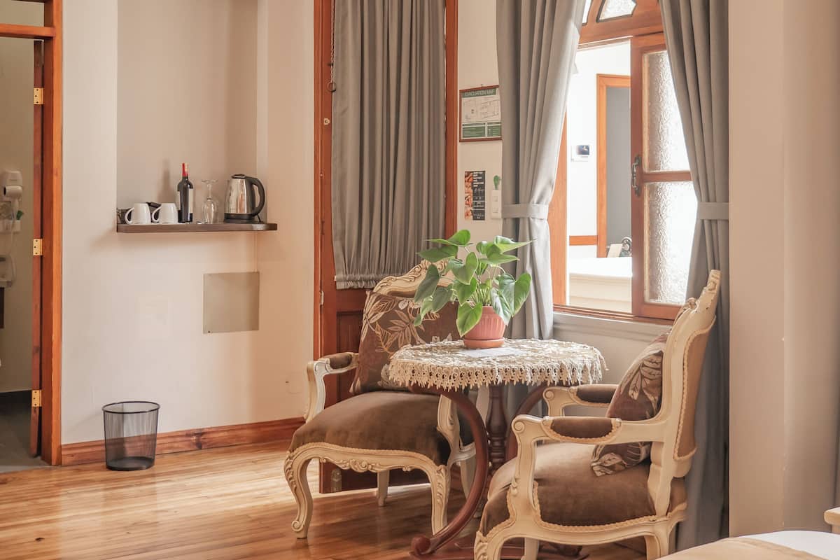 A cozy room with a wooden floor, a round table with chairs, a potted plant, and a window with curtains.