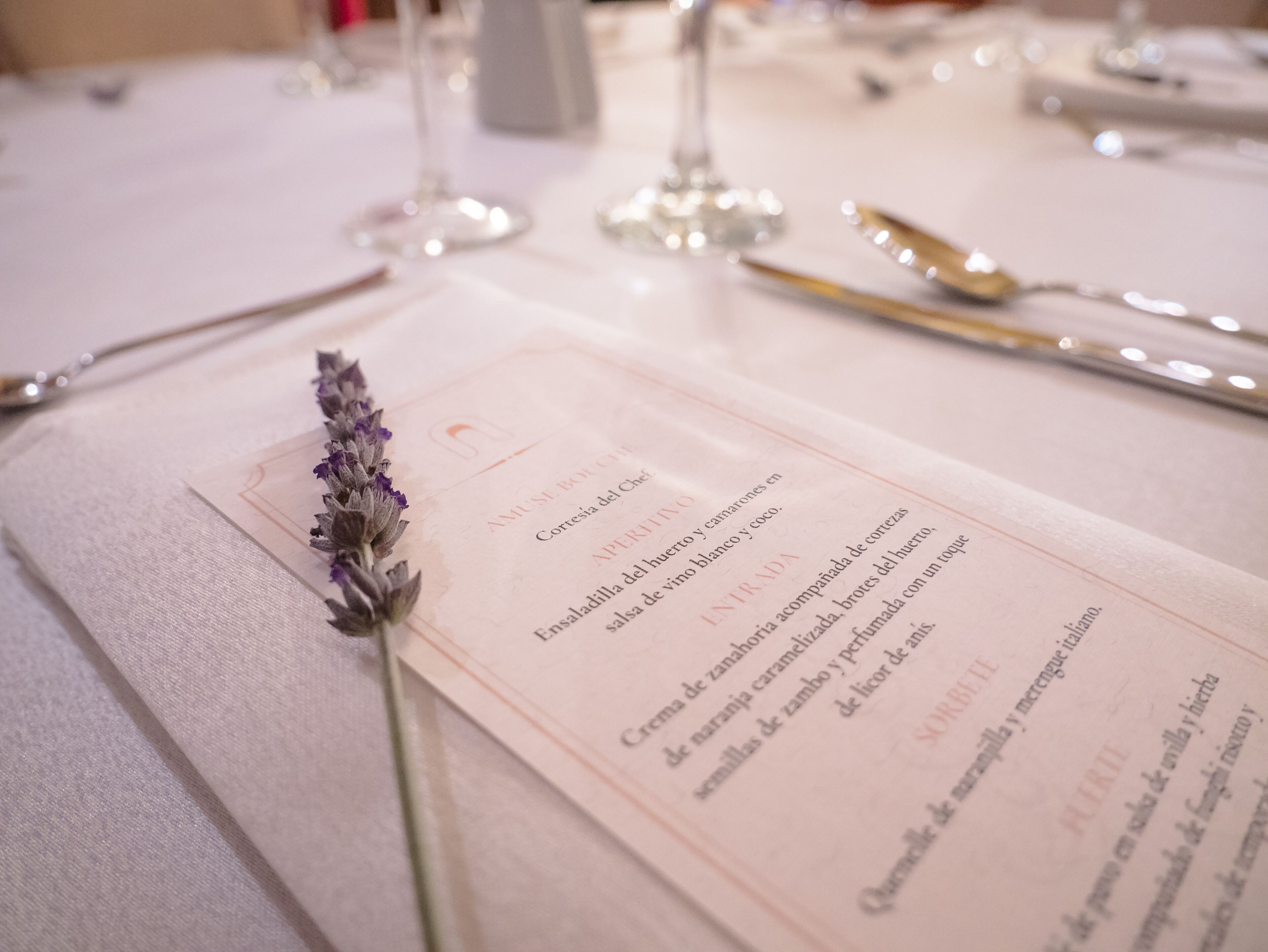 Un menú con adorno de lavanda sobre una mesa dispuesta para comer.
