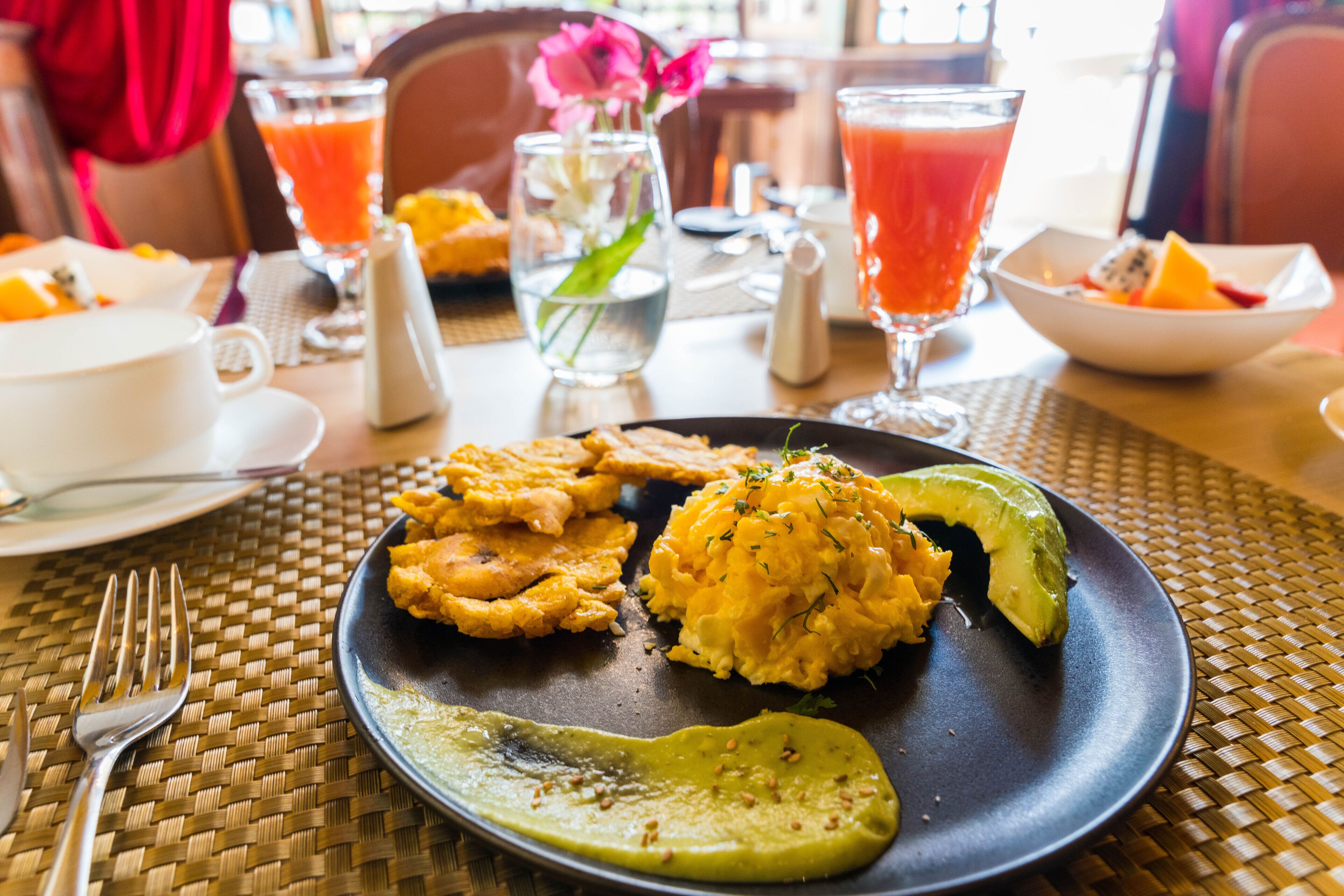 A dining table with a plate of food, including avocado and scrambled eggs, and two glasses of orange juice.