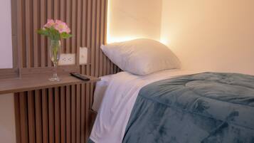 A hotel room with a wooden slat wall, a bedside table with a vase of flowers, a remote control, and a bed with a white pillow and blue blanket.
