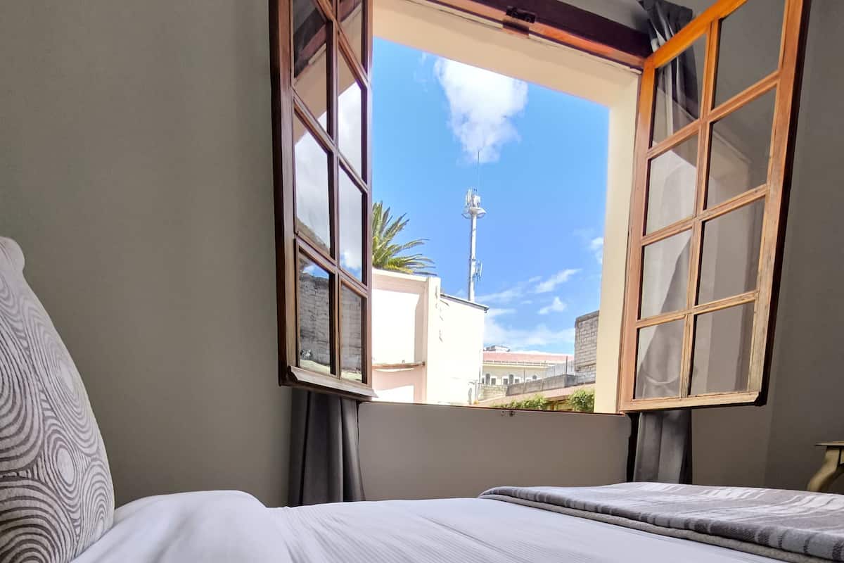 A bedroom with a bed, a window, and a view of the outside.