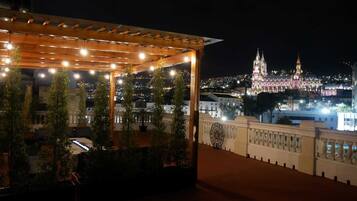 Une terrasse sur le toit, agrémentée de guirlandes lumineuses, de plantes en pot et offrant une vue sur la ville, avec ses bâtiments illuminés la nuit.