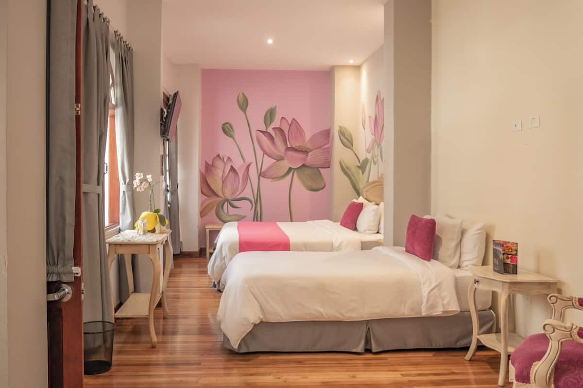 A hotel room with two beds, a small table, a chair, and a wall with a floral mural.